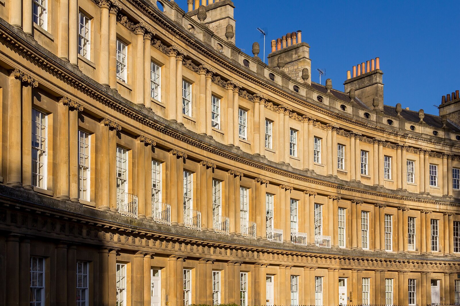 The Circus in Bath - a sweeping curved terrace of Georgian stone townhouses with columns, honey-coloured in golden light