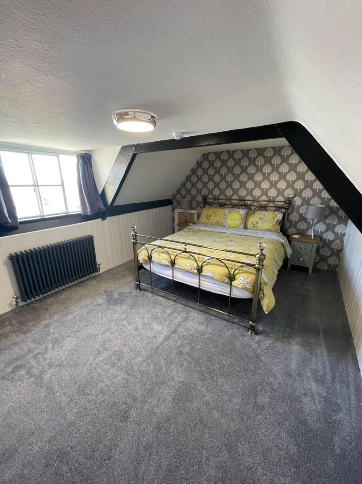 Characterful period guest bedroom with brass bedstead, soft yellow bedding, exposed beams and sash window