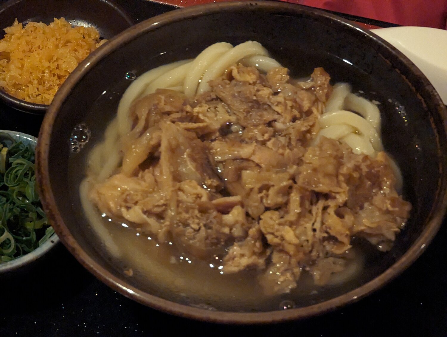 Bowl of Japanese udon noodle soup with sliced beef, spring onions and tempura flakes