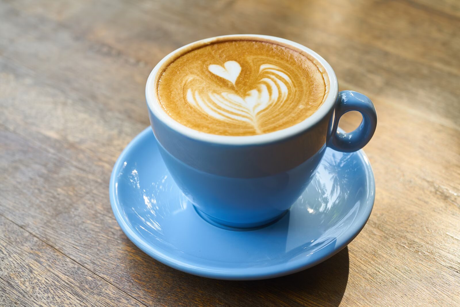 A flat white with leaf latte art in a blue cup and saucer on a wooden table