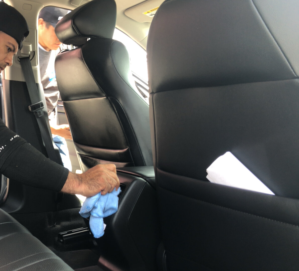 Interior valeting - hand wiping black leather car seats with blue microfibre cloth inside clean car cabin