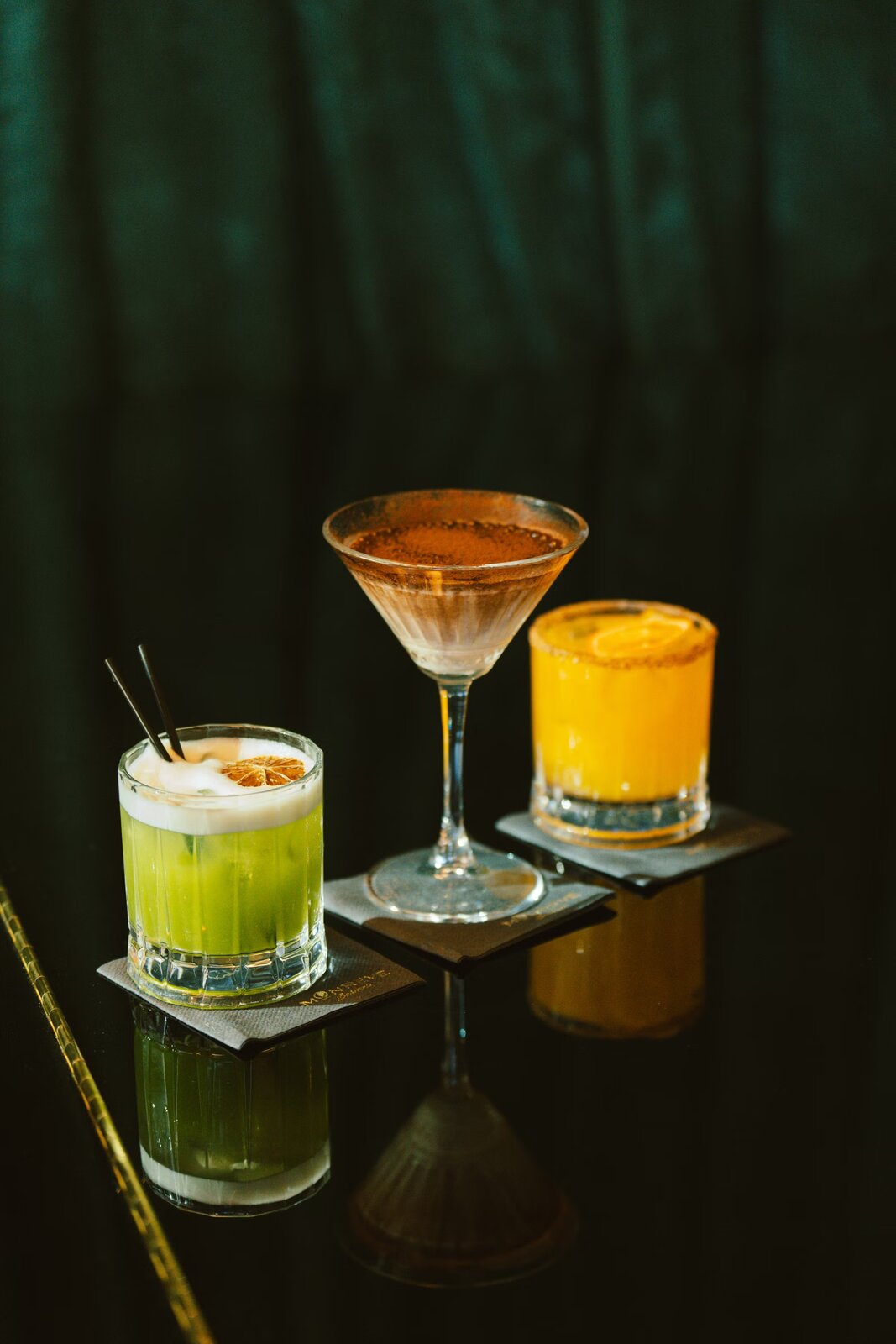 A trio of elegant cocktails on a dark candlelit bar top